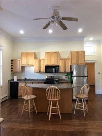 kitchen with stainless steel appliances, ornamental molding, a breakfast bar area, light brown cabinetry, and a kitchen island