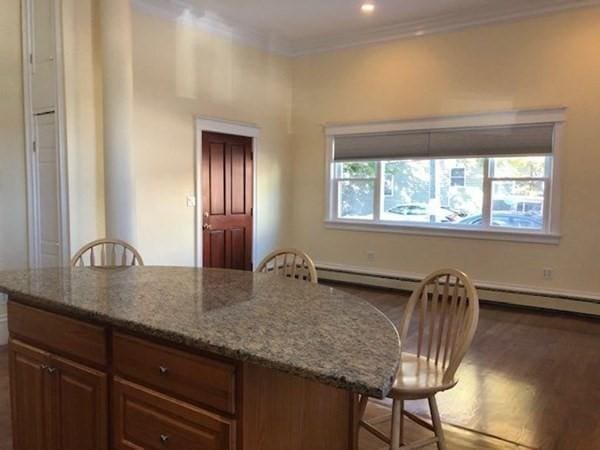 kitchen with crown molding, wood finished floors, light stone counters, a breakfast bar, and a center island