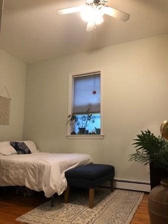 bedroom featuring wood finished floors, a baseboard heating unit, and ceiling fan
