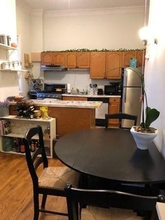 kitchen featuring appliances with stainless steel finishes, under cabinet range hood, ornamental molding, light wood-style floors, and light countertops