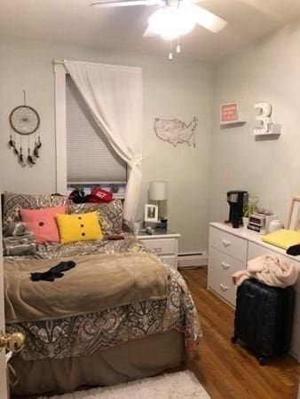bedroom with wood finished floors, a baseboard radiator, and a ceiling fan