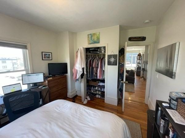 bedroom featuring wood finished floors, a closet, an office area, and baseboards