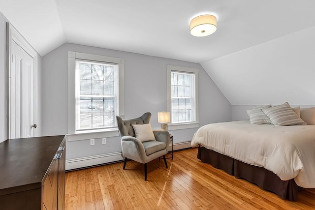 bedroom featuring a baseboard heating unit, lofted ceiling, and light wood-style flooring