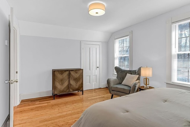 bedroom featuring vaulted ceiling, baseboards, light wood-type flooring, and a closet