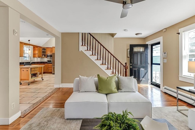 living area featuring stairs, baseboards, light wood-type flooring, and a baseboard radiator