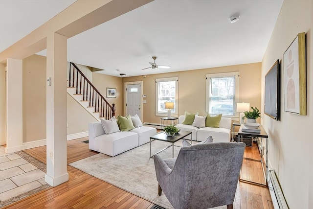 living area featuring baseboards, stairs, baseboard heating, light wood-style floors, and a baseboard radiator