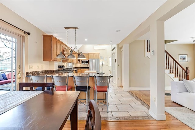 kitchen with light wood finished floors, decorative light fixtures, an AC wall unit, appliances with stainless steel finishes, and a peninsula