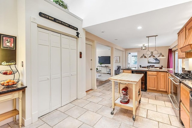 kitchen featuring beverage cooler, gas stove, a peninsula, dark countertops, and decorative light fixtures