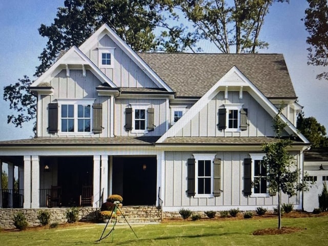 view of front of property with board and batten siding, a front yard, and roof with shingles