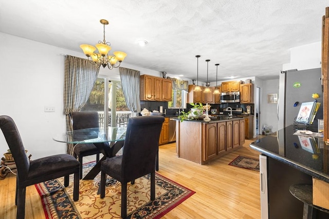 dining room with a textured ceiling, sink, a chandelier, and light hardwood / wood-style flooring