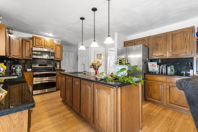 kitchen featuring an island with sink, appliances with stainless steel finishes, tasteful backsplash, pendant lighting, and sink