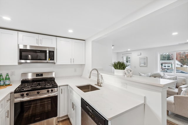 kitchen with white cabinetry, sink, stainless steel appliances, kitchen peninsula, and light hardwood / wood-style floors