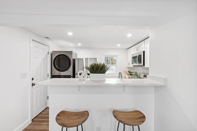 kitchen with stacked washer / drying machine, a kitchen breakfast bar, kitchen peninsula, and stainless steel appliances