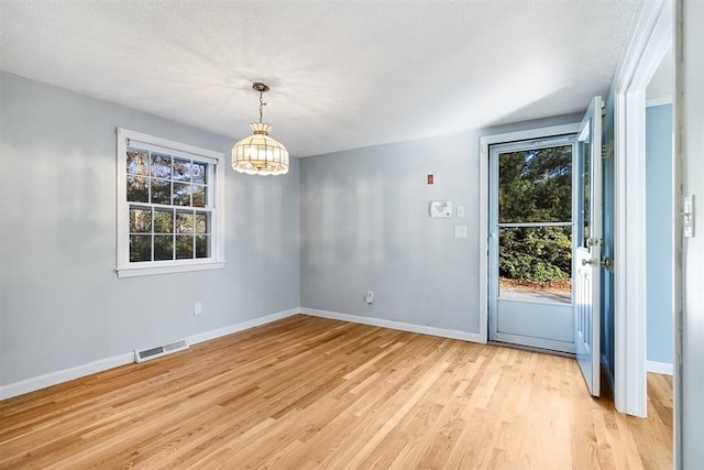 unfurnished dining area featuring a wealth of natural light, light hardwood / wood-style flooring, and a textured ceiling