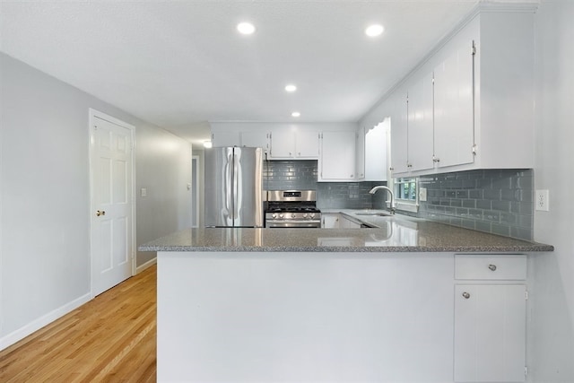 kitchen with white cabinets, kitchen peninsula, stainless steel appliances, and light hardwood / wood-style flooring