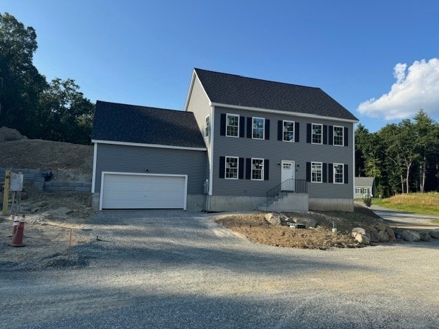 colonial inspired home with an attached garage and gravel driveway