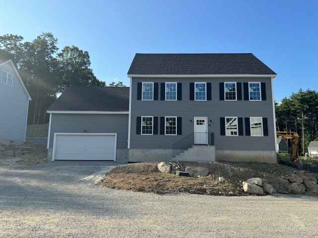 colonial inspired home featuring a garage and gravel driveway