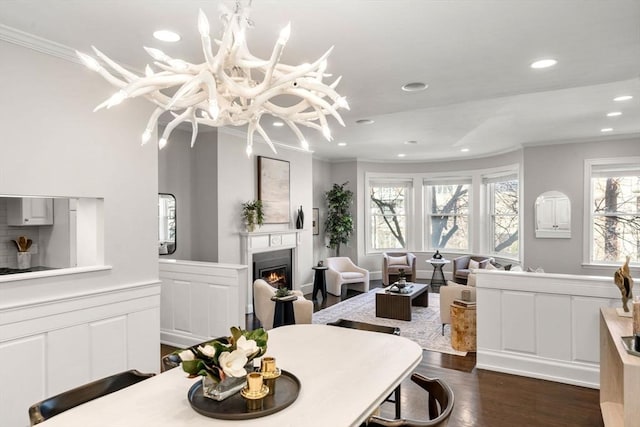 dining room featuring a wainscoted wall, a warm lit fireplace, ornamental molding, and dark wood-style flooring