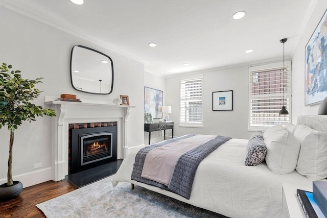 bedroom with a glass covered fireplace, wood finished floors, recessed lighting, crown molding, and baseboards