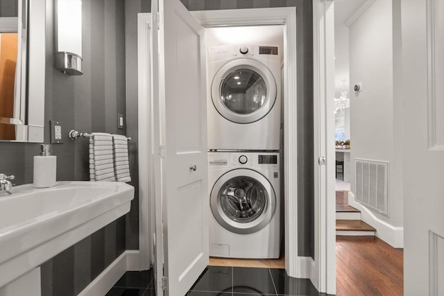 washroom with visible vents, stacked washer and clothes dryer, a sink, laundry area, and dark wood-style flooring