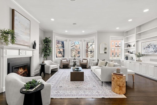 living room with built in features, dark wood-type flooring, a glass covered fireplace, and crown molding