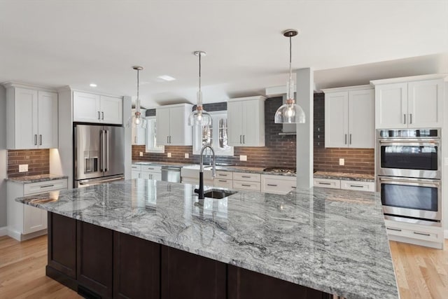 kitchen with appliances with stainless steel finishes, white cabinets, a sink, and light wood finished floors