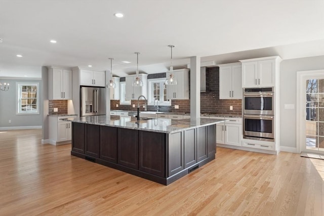 kitchen featuring light wood-style flooring, an inviting chandelier, stainless steel appliances, a large island with sink, and a sink