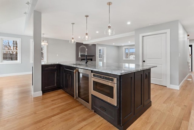 kitchen with wine cooler, a sink, baseboards, light wood-type flooring, and stainless steel microwave