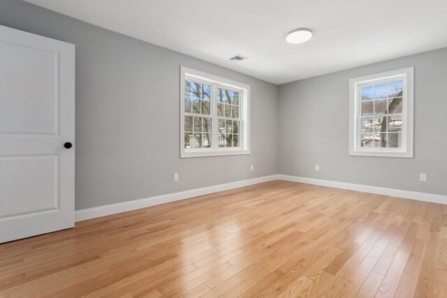 empty room with light wood-type flooring, visible vents, and baseboards