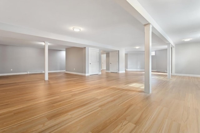 finished below grade area with light wood finished floors, a baseboard radiator, and baseboards