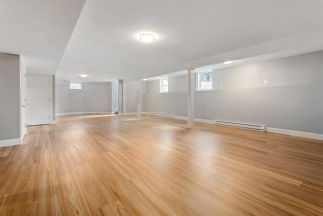 basement with light wood-style floors, a baseboard radiator, baseboards, and a baseboard heating unit