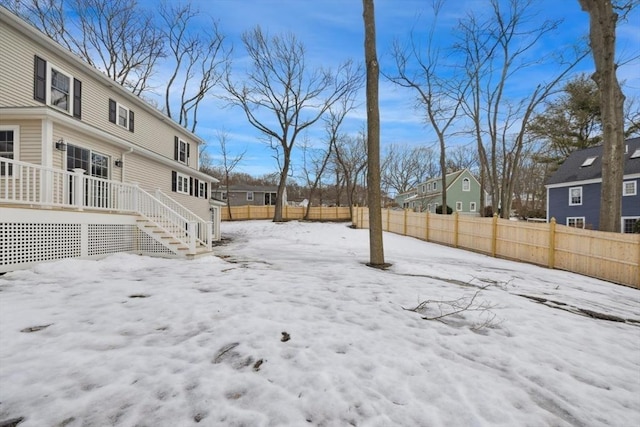 yard covered in snow with a residential view, a fenced backyard, a deck, and stairs