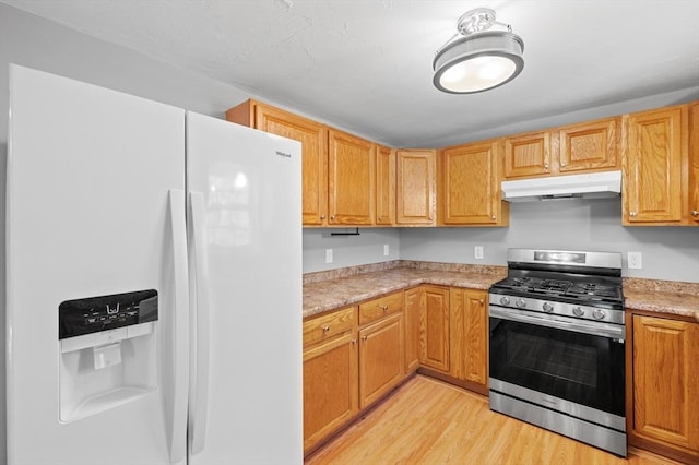 kitchen with stainless steel range with gas stovetop, white refrigerator with ice dispenser, light countertops, light wood-style floors, and under cabinet range hood