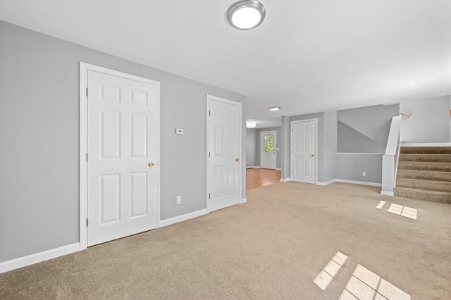 unfurnished living room featuring stairs, baseboards, and light carpet