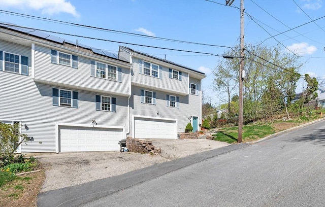townhome / multi-family property with a garage, roof mounted solar panels, and aphalt driveway