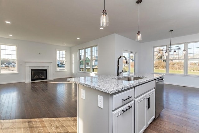 kitchen featuring a center island with sink, stainless steel dishwasher, sink, and hanging light fixtures