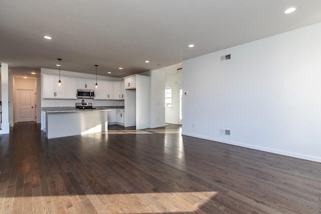 kitchen featuring stove, a kitchen island with sink, decorative light fixtures, dark hardwood / wood-style flooring, and white cabinetry