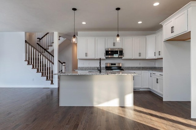 kitchen featuring white cabinetry, light stone countertops, stainless steel appliances, and an island with sink