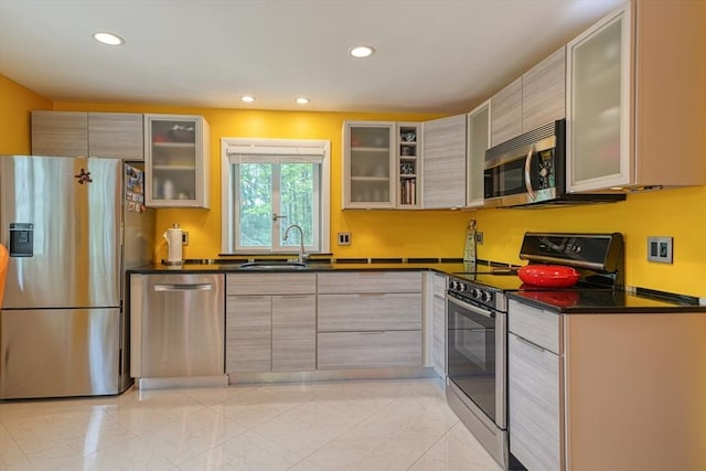 kitchen with appliances with stainless steel finishes, a sink, dark countertops, recessed lighting, and glass insert cabinets
