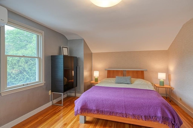 bedroom featuring lofted ceiling, light wood-style flooring, baseboards, and a wall mounted AC