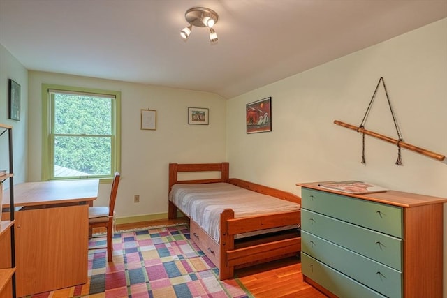 bedroom featuring baseboards, light wood finished floors, and vaulted ceiling