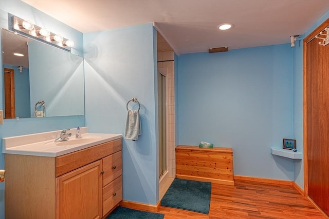 bathroom with wood finished floors, vanity, a stall shower, baseboards, and recessed lighting