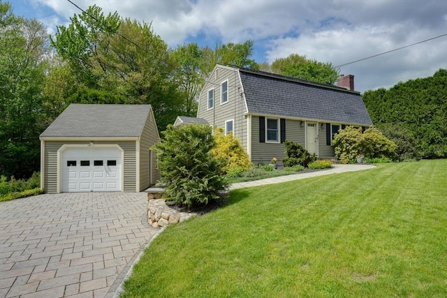 colonial inspired home featuring an outbuilding, a gambrel roof, a chimney, decorative driveway, and a front lawn