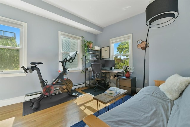 exercise room featuring a baseboard radiator, baseboards, and wood finished floors