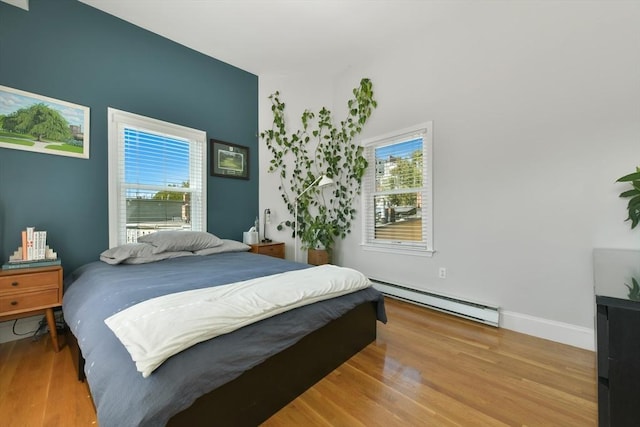 bedroom featuring baseboards, multiple windows, a baseboard heating unit, and wood finished floors