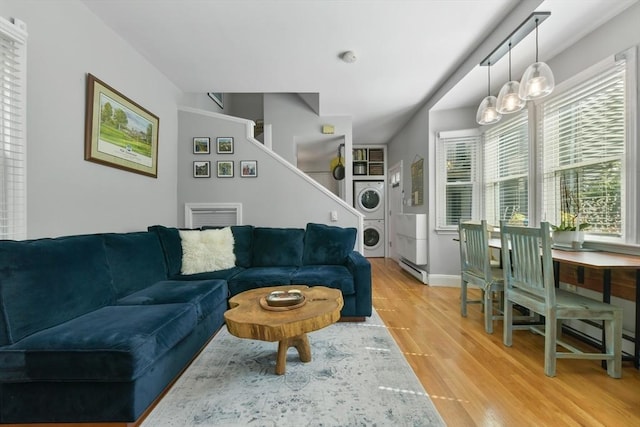 living area with baseboards, stacked washer and dryer, light wood-style flooring, and a healthy amount of sunlight