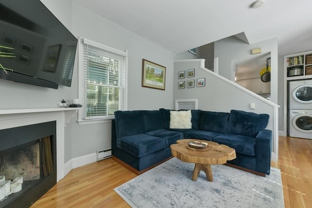 living area with stacked washer and dryer, a fireplace, wood finished floors, baseboards, and baseboard heating