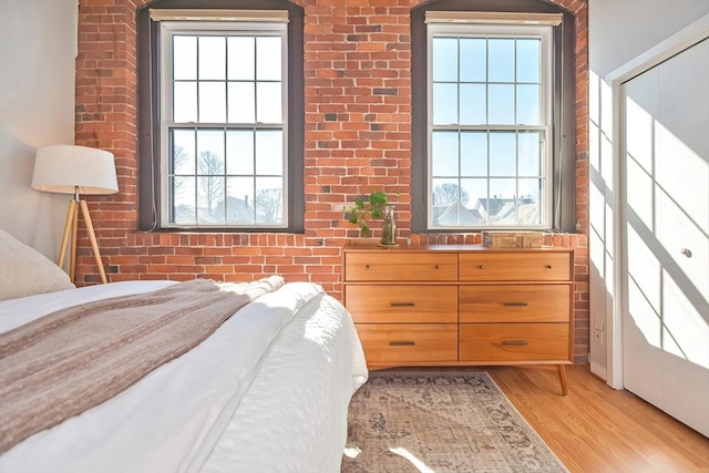 bedroom featuring light wood-type flooring and brick wall