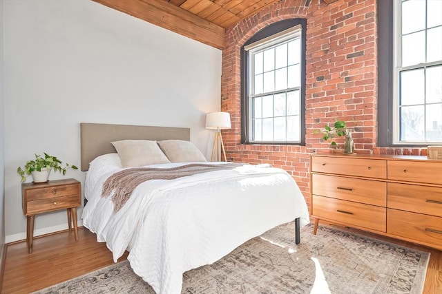 bedroom with beam ceiling, wood finished floors, wood ceiling, and brick wall