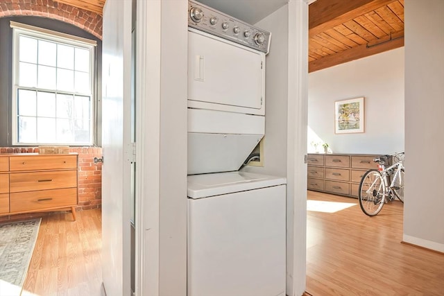 washroom featuring baseboards, laundry area, wood ceiling, stacked washer / dryer, and light wood-type flooring